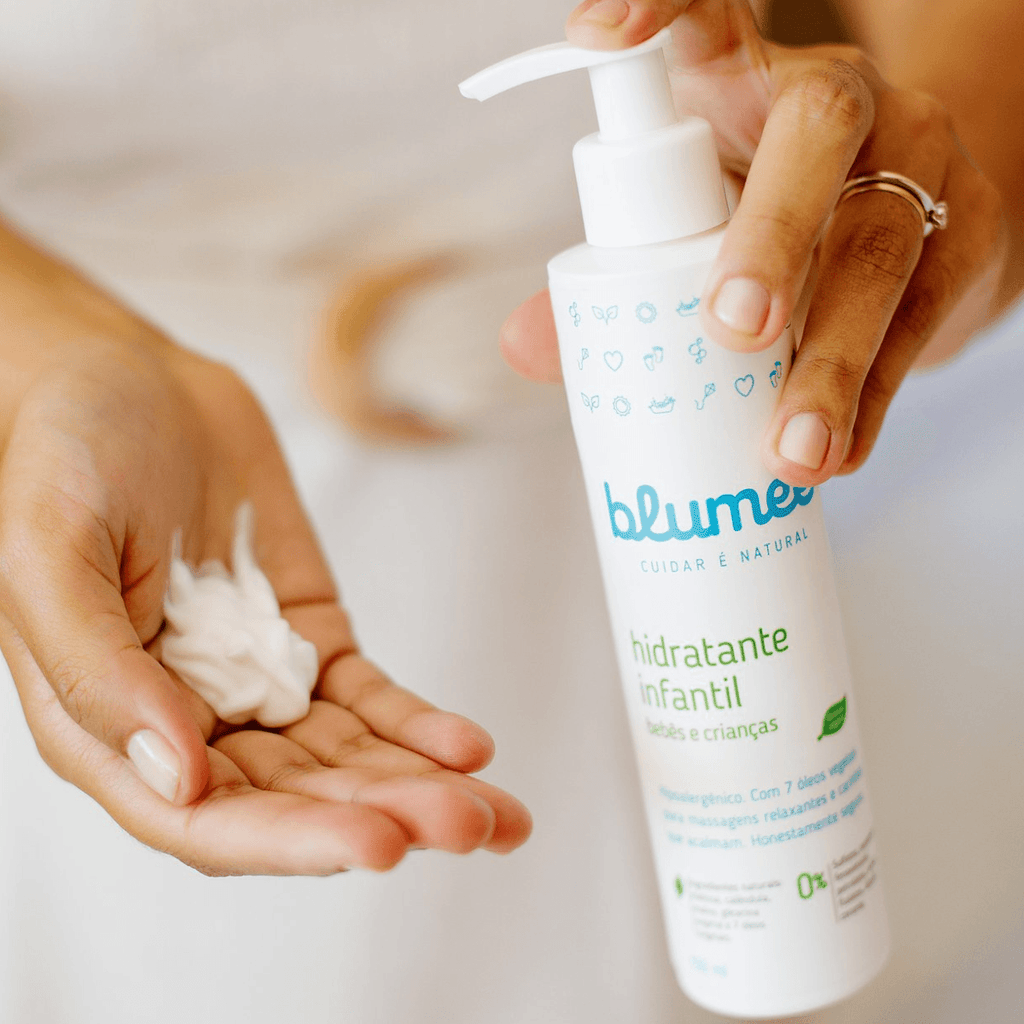 Mãos aplicando Hidratante Infantil Blumee, textura cremosa na palma da mão