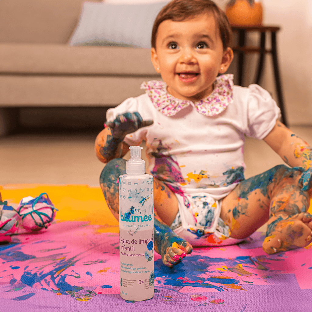 Bebê brincando com tintas coloridas ao lado da Água de Limpeza Blumee, higiene divertida