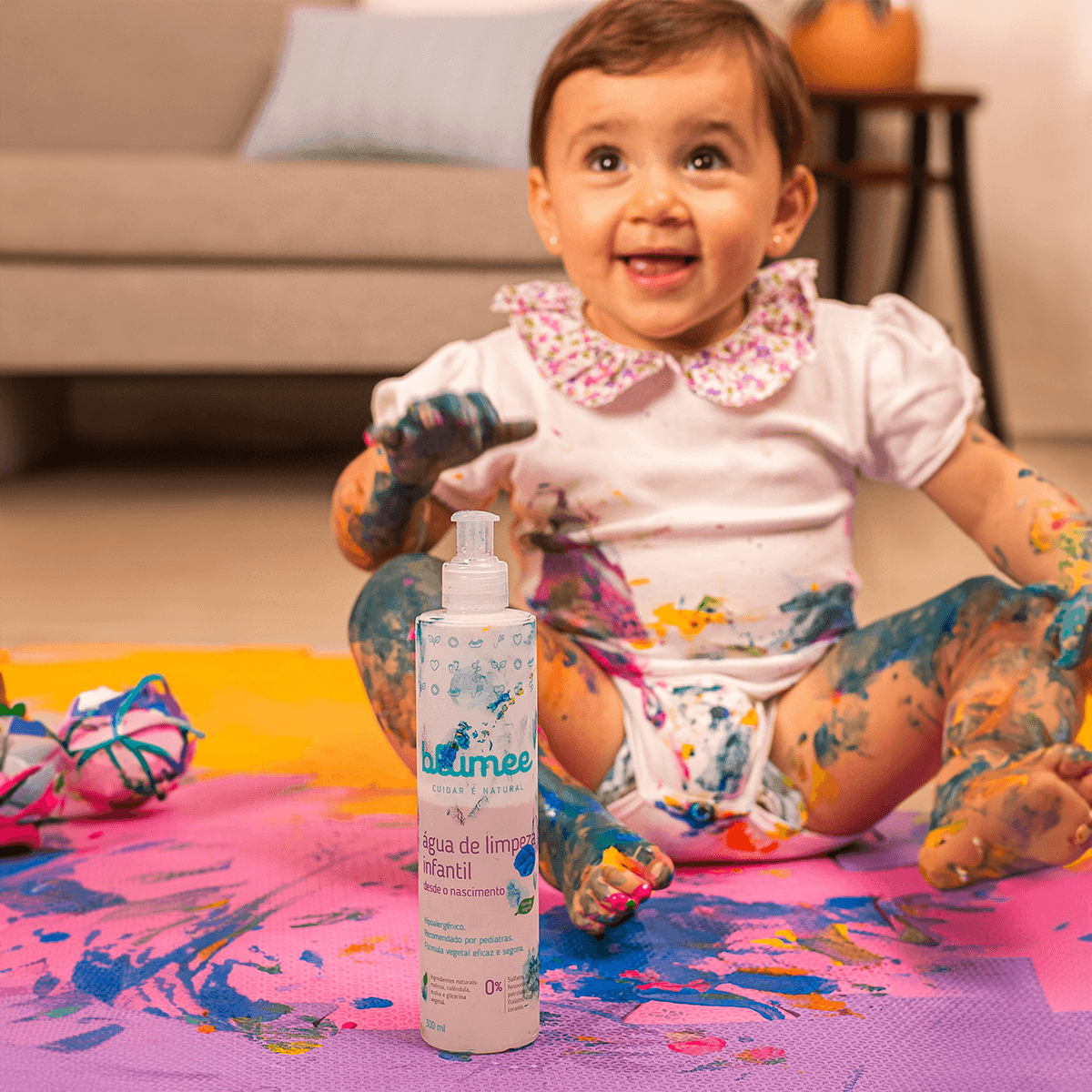 Bebê brincando com tintas coloridas ao lado da Água de Limpeza Blumee, higiene divertida