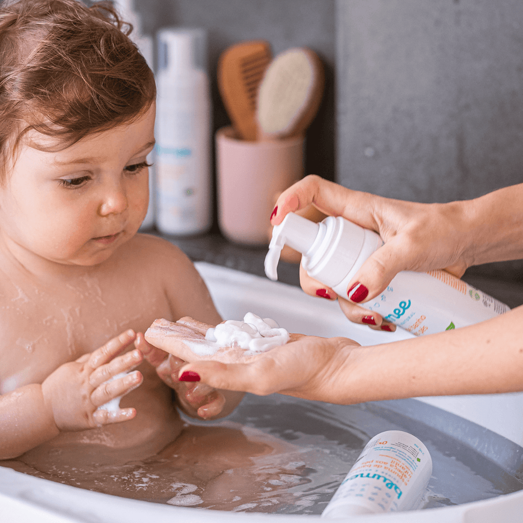 Mãe aplicando espuma de banho Blumee na mão do bebê durante o banho