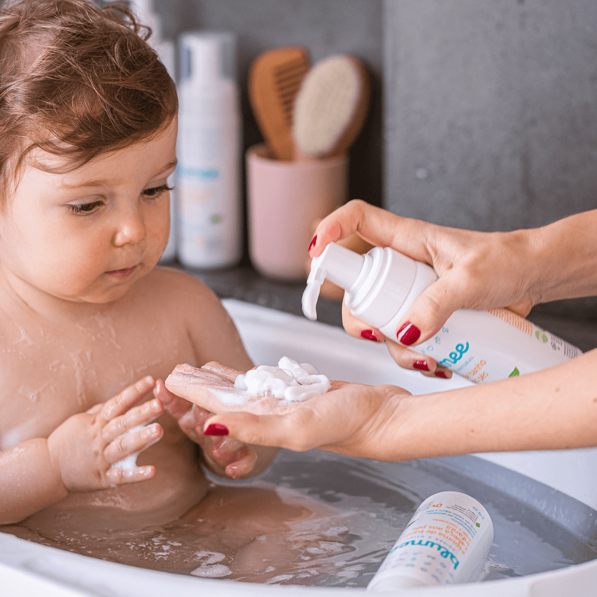 Mãe aplicando espuma de banho Blumee na mão do bebê durante o banho