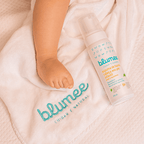 Espuma de Banho Blumee 210ml ao lado do pezinho de bebê sobre toalha branca