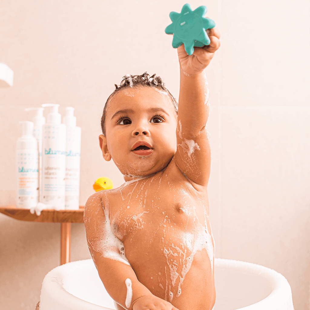 Bebê sorrindo com espuma na cabeça segurando brinquedo, banho com Blumee