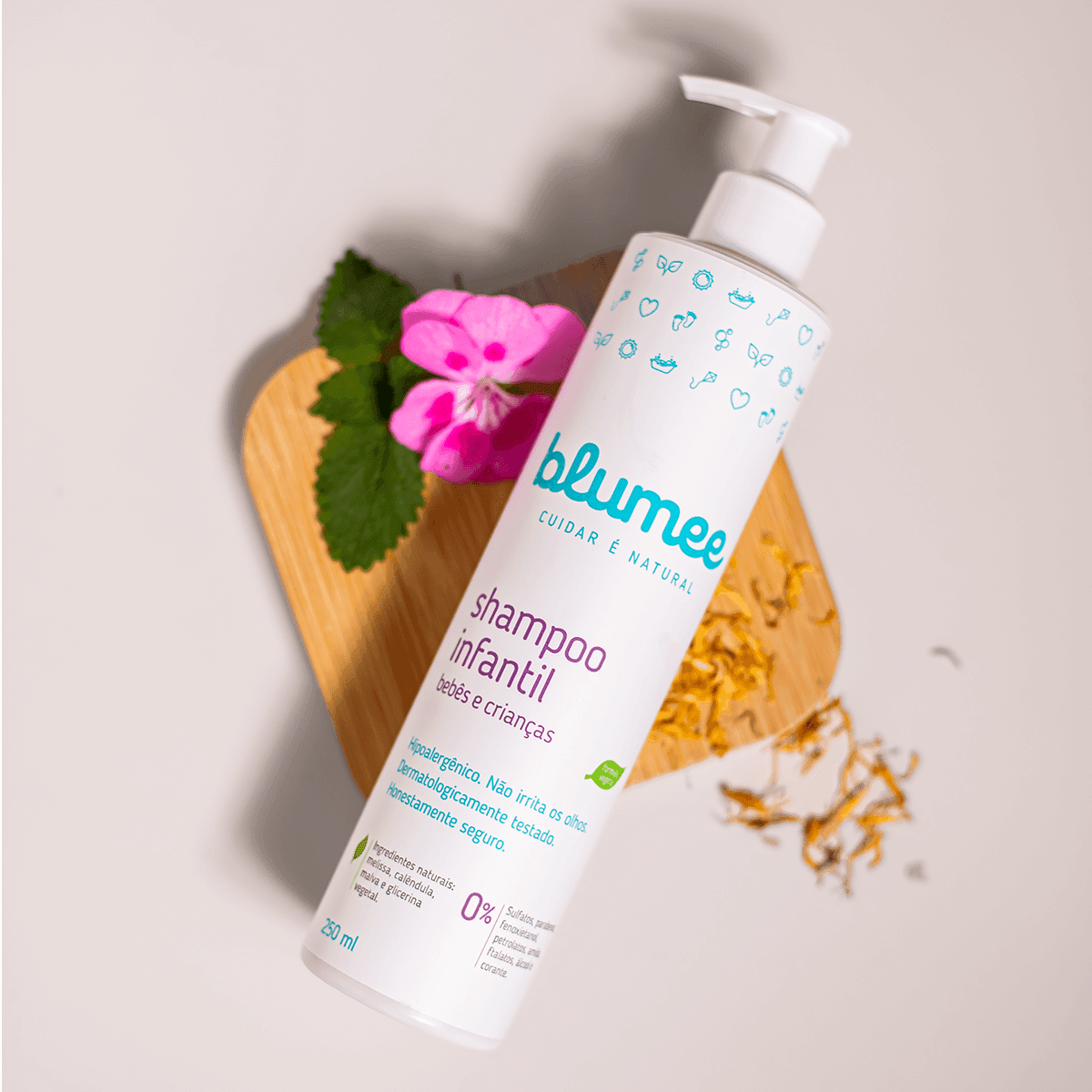 Shampoo Infantil Blumee 250ml em still com flor rosa e ervas sobre madeira