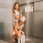 Duas crianças lavando o cabelo juntas no chuveiro com produtos do Kit Trio Blumee