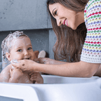 Mãe sorridente lavando o cabelo do bebê com produtos do Kit Mamãe & Bebê